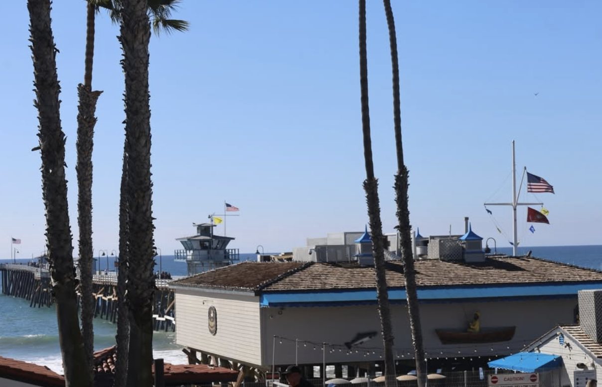Palm trees and the San Clemente Pier against a clear blue sky, just down the street from Frenchies Cafe